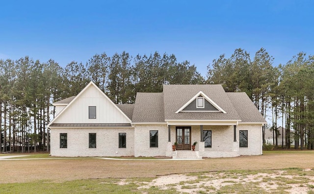 view of front facade featuring a front yard, covered porch, roof with shingles, and brick siding