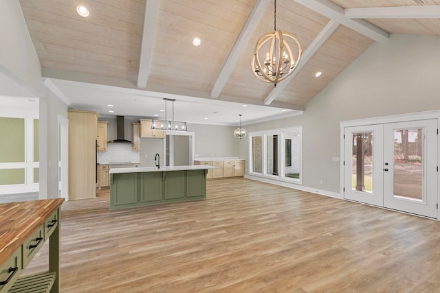 kitchen featuring green cabinetry, a notable chandelier, light countertops, wall chimney range hood, and a sink