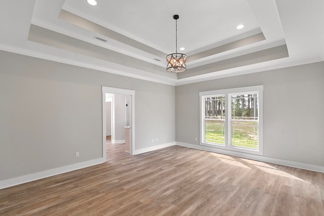 empty room with light wood-style floors, a tray ceiling, and baseboards