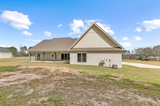 back of property with board and batten siding, a patio area, brick siding, and a yard