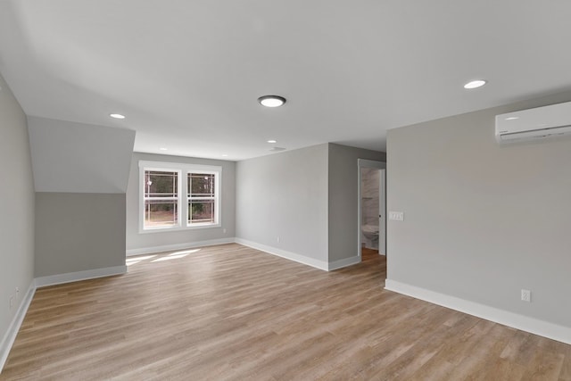 empty room featuring baseboards, recessed lighting, a wall unit AC, and light wood-style floors