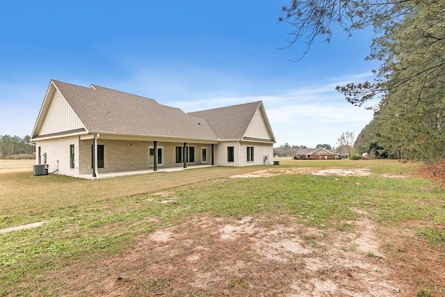 rear view of property with central AC, brick siding, a shingled roof, a yard, and a patio area