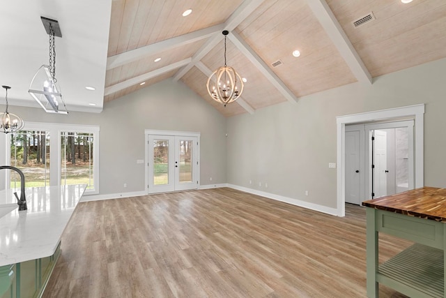 unfurnished living room with french doors, light wood-style floors, beamed ceiling, and an inviting chandelier