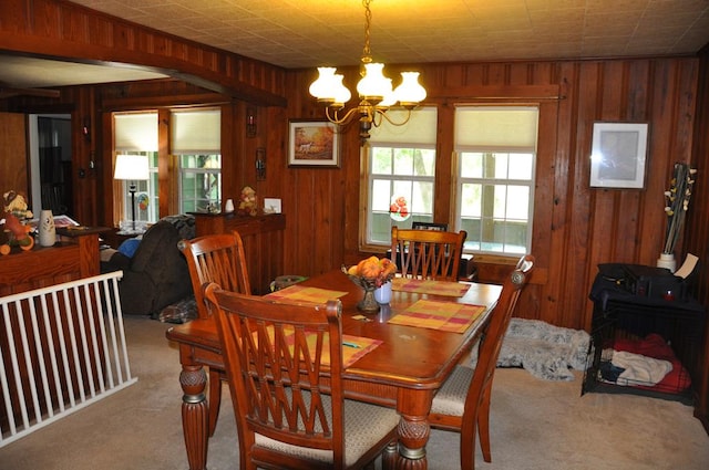 dining space with a notable chandelier, wood walls, and light colored carpet