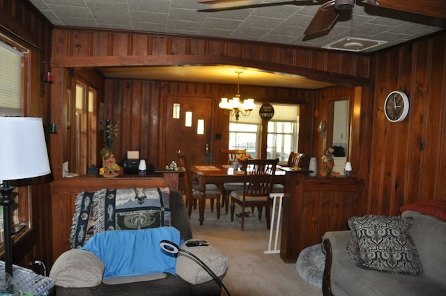 carpeted dining area with wooden walls and ceiling fan with notable chandelier