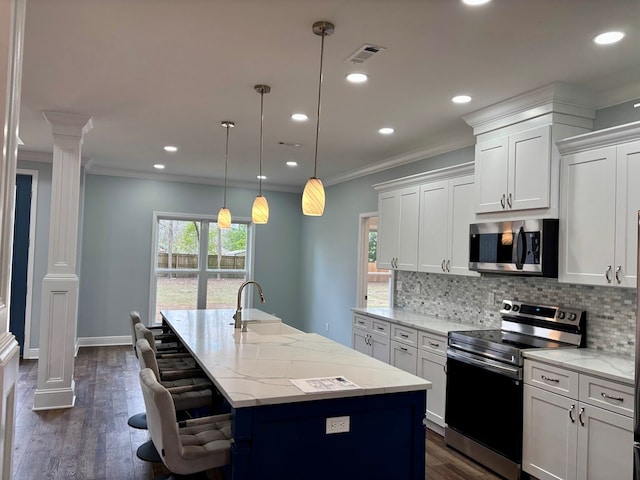 kitchen with pendant lighting, sink, appliances with stainless steel finishes, white cabinetry, and a center island with sink