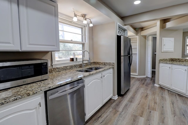 kitchen with appliances with stainless steel finishes, white cabinetry, light stone countertops, and sink