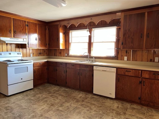 kitchen featuring a sink, wood walls, white appliances, light countertops, and under cabinet range hood