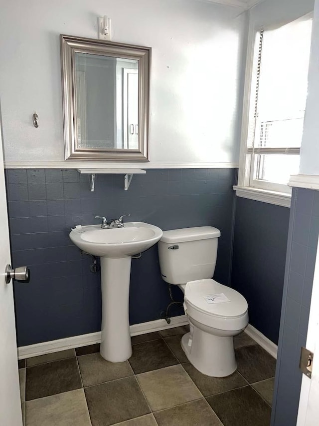 half bath with wainscoting, tile walls, tile patterned flooring, and toilet