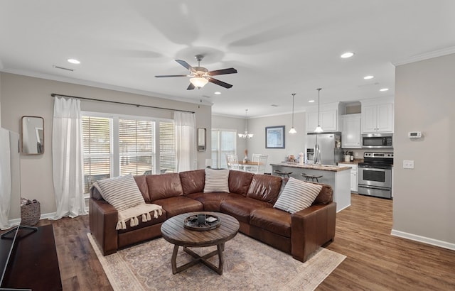 living room featuring hardwood / wood-style floors, crown molding, and ceiling fan with notable chandelier