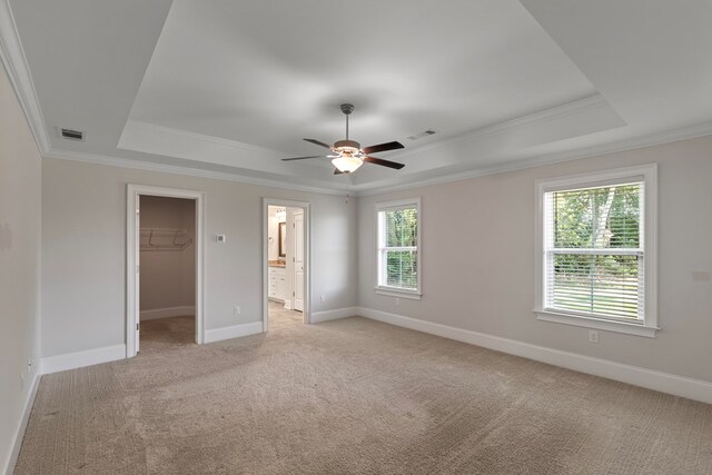 unfurnished bedroom featuring a raised ceiling, a walk in closet, ceiling fan, and light carpet