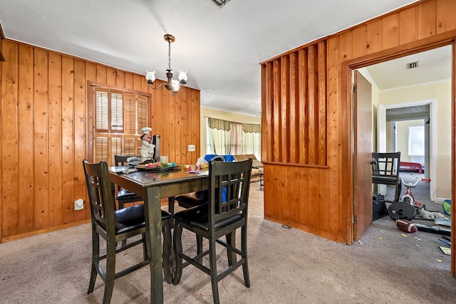 dining area featuring a chandelier, light colored carpet, wood walls, and visible vents