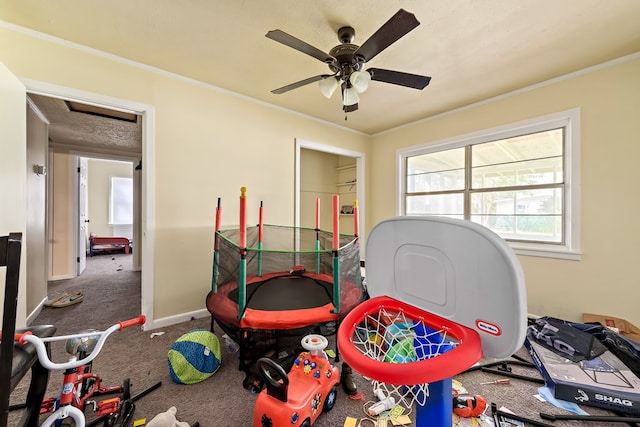 recreation room with ornamental molding, carpet flooring, ceiling fan, and baseboards