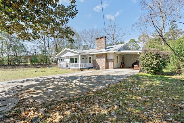 back of property with a porch, aphalt driveway, brick siding, a lawn, and a chimney