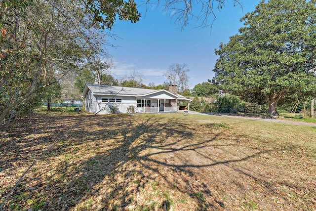 back of house with a porch, a yard, and a chimney