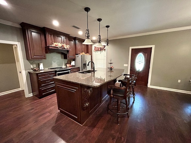 kitchen with dark brown cabinets, stainless steel appliances, a kitchen island with sink, dark wood-type flooring, and pendant lighting