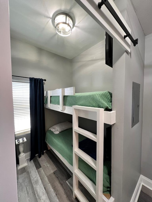 bedroom with baseboards, electric panel, and wood finished floors