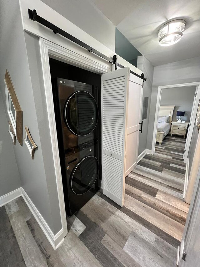 clothes washing area with laundry area, wood finished floors, baseboards, a barn door, and stacked washer / drying machine