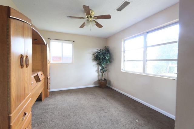 unfurnished bedroom with multiple windows, ceiling fan, and dark carpet