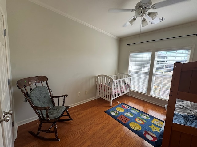 bedroom featuring ceiling fan, wood finished floors, visible vents, baseboards, and ornamental molding