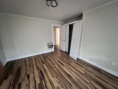 unfurnished bedroom with heating unit, dark hardwood / wood-style floors, a closet, and crown molding