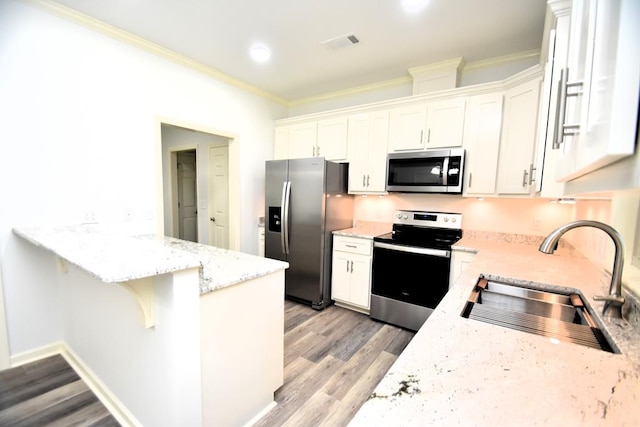 kitchen featuring appliances with stainless steel finishes, ornamental molding, sink, light hardwood / wood-style flooring, and white cabinets