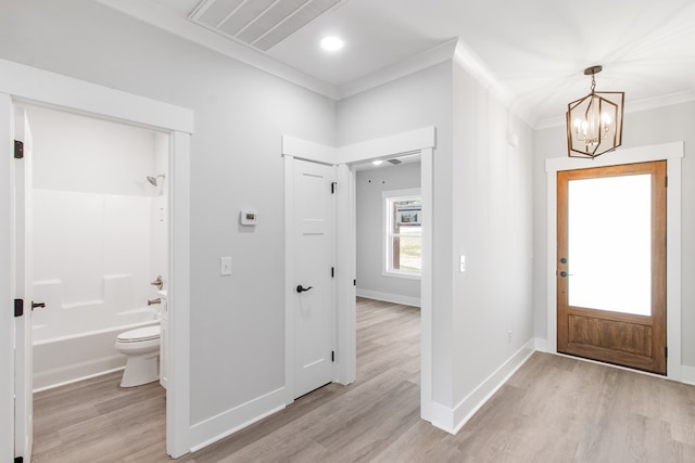 entryway with light hardwood / wood-style floors, crown molding, and an inviting chandelier