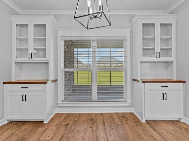 unfurnished dining area featuring a chandelier, light wood-style flooring, baseboards, and ornamental molding