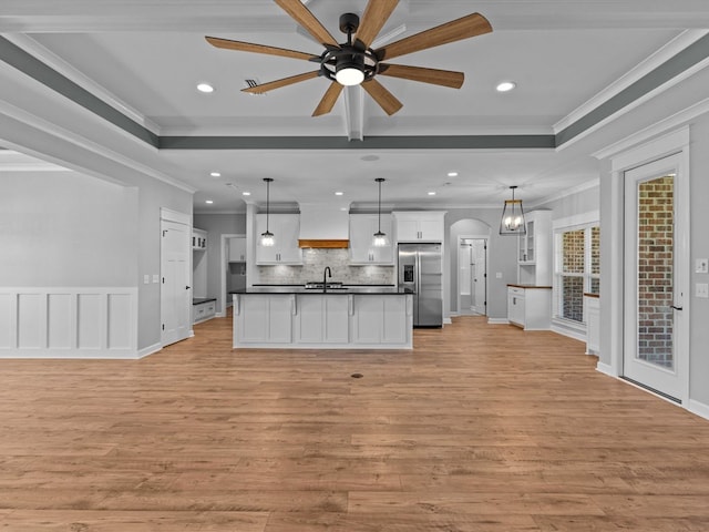 kitchen featuring stainless steel refrigerator with ice dispenser, open floor plan, dark countertops, a sink, and ornamental molding