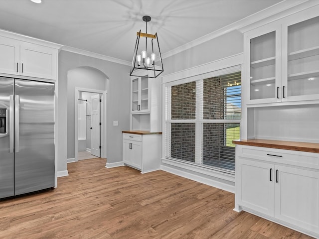 unfurnished dining area featuring arched walkways, crown molding, light wood finished floors, a chandelier, and baseboards