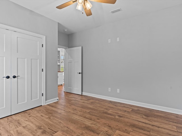 unfurnished bedroom featuring wood finished floors, baseboards, ceiling fan, and a closet