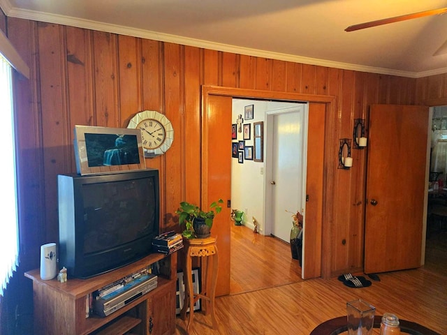 living room with ceiling fan, wood walls, wood-type flooring, and ornamental molding