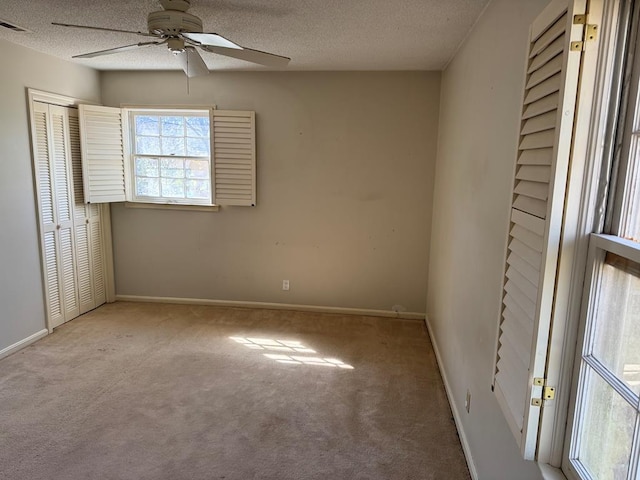 empty room featuring light colored carpet, ceiling fan, a textured ceiling, and baseboards