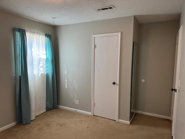 unfurnished bedroom with baseboards, visible vents, a textured ceiling, and light colored carpet