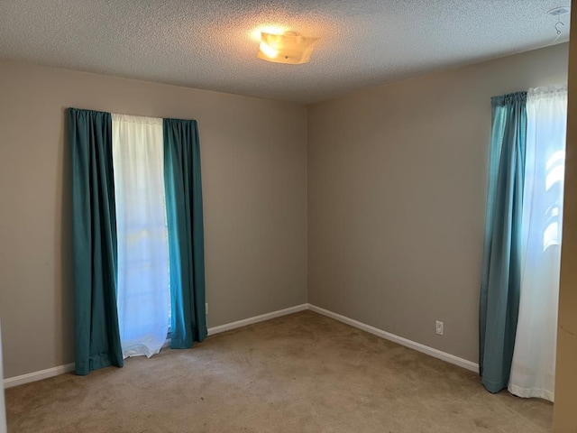 unfurnished room with light carpet, baseboards, and a textured ceiling