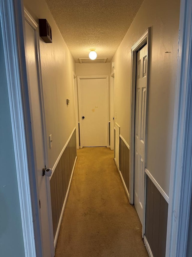 hallway with a textured ceiling, wainscoting, and carpet flooring