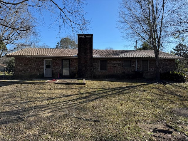 back of house featuring a chimney, metal roof, a lawn, and brick siding