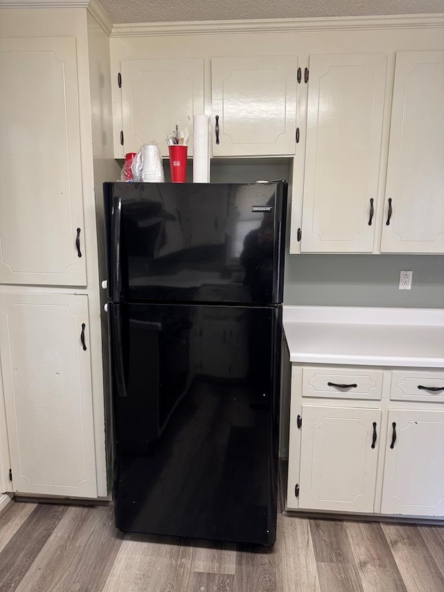 kitchen with light wood-type flooring, freestanding refrigerator, white cabinets, and light countertops