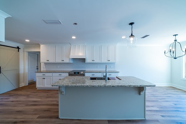 kitchen featuring a barn door, white cabinets, decorative light fixtures, a kitchen island with sink, and a sink