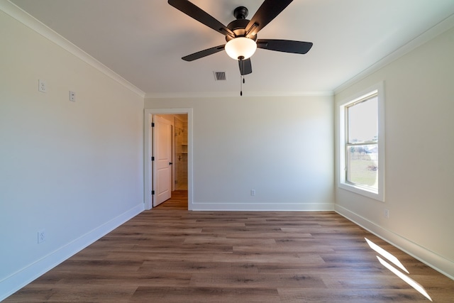 empty room featuring baseboards, wood finished floors, visible vents, and crown molding