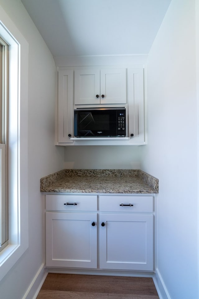 bar featuring black microwave, dark wood finished floors, and baseboards