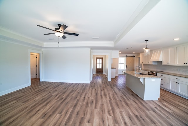 kitchen with a barn door, white cabinets, a raised ceiling, a kitchen breakfast bar, and a kitchen island with sink