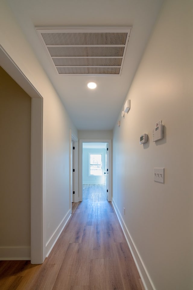 hall with light wood-type flooring, visible vents, and baseboards