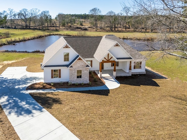 modern farmhouse style home featuring stone siding, a shingled roof, a front lawn, and covered porch