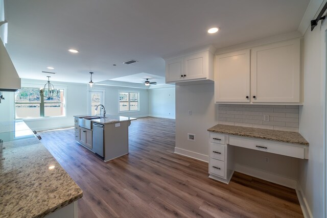 kitchen with white cabinets, open floor plan, hanging light fixtures, light stone countertops, and an island with sink