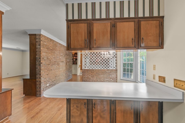 kitchen with light countertops, decorative columns, a peninsula, brown cabinets, and light wood finished floors