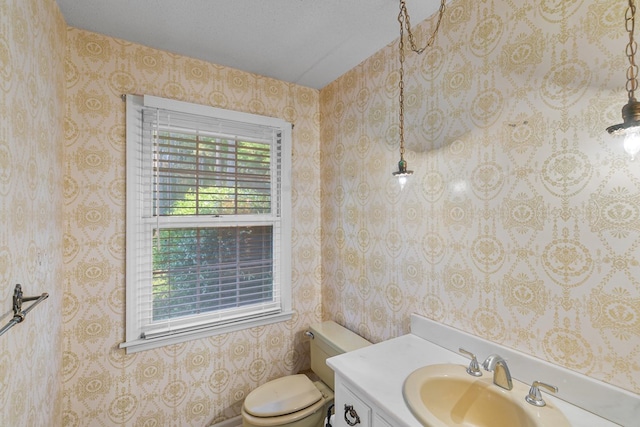 half bathroom with vanity, wallpapered walls, and toilet