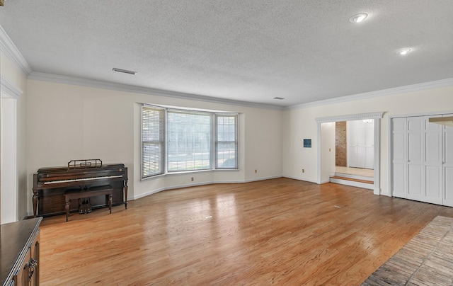 unfurnished living room featuring baseboards, ornamental molding, a textured ceiling, light wood-style floors, and visible vents