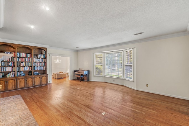 interior space with a textured ceiling, wood finished floors, crown molding, and visible vents