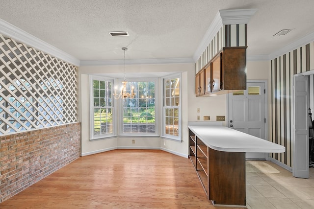 kitchen with visible vents, a notable chandelier, brick wall, light countertops, and a peninsula